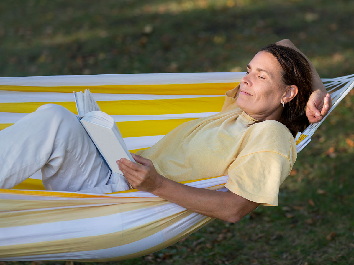 A woman relaxes in a hammock, engrossed in a book on a sunny day