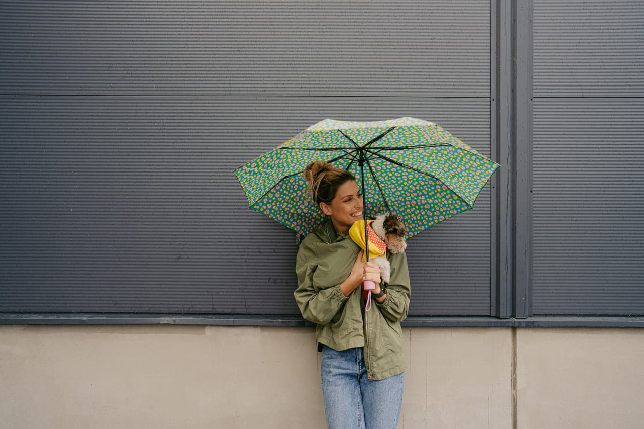 A woman stands outdoors, holding a colorful umbrella against a cloudy sky